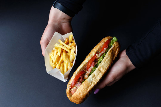 Hot dog and French fries in the hands on the black background.
