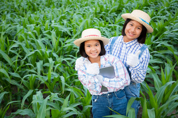 Two little girl consulting and pointed to product tracking in corn field. She’s fresh smile and happiness in the evening. Corn products are used to produce food for humans and animals. Growth concept