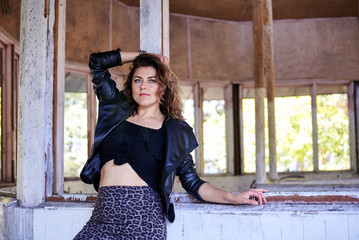 Young brunette woman, wearing black top with leather jacket and dark long skirt and high heels, posing in old abandoned building. Urban lifestyle female photo session.