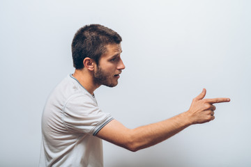 Closeup side view portrait of young man, pointing with finger at someone or something. Positive human face expressions, emotions, feelings, attitude, approach