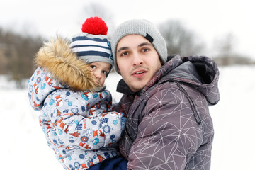 Fototapeta premium Happy dad holding his son, little funny kid boy on arm, on cold day, walking together in a park in spring, autumn or winter. Happy, joyful family.