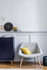 Interior design of living room with stylish navy blue commode, grey armchair, pillow, black clock, dried flower, modern paintings, decoration and elegant accessories in home decor.
