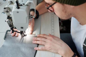 Hands of young leatherworker sewing zipper and piece of leather together