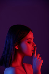 Pretty young brunette woman holding forefinger by her mouth expressing quietness