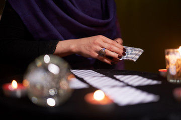 Fortune teller woman in purple dress divines on cards sitting at table with candles