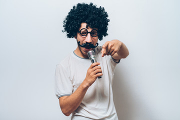 A man in a wig and funny glasses, singing into the microphone