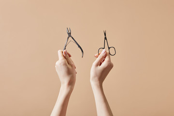 Cropped view of woman holding cuticle nipper and nail scissors isolated on beige