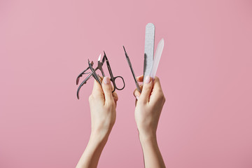 Cropped view of woman holding manicure instruments isolated on pink