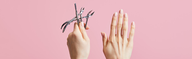 Cropped view of woman holding cuticle pusher and nippers isolated on pink, panoramic shot - obrazy, fototapety, plakaty