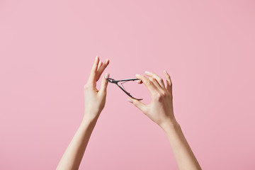 Cropped view of woman cutting cuticle with nipper isolated on pink