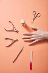 Cropped view of female hand with bottle of nail polish and manicure instruments on coral