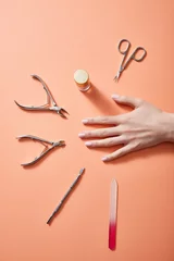 Gordijnen Cropped view of female hand with bottle of nail polish and manicure instruments on coral © LIGHTFIELD STUDIOS