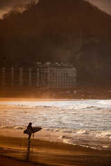 Surfer silhouette walking on an empty beach during golden hour