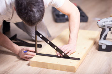 A man with dark hair measures a console and a wooden shelf on the floor at home, close-up