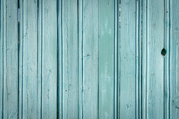 Background in grunge style. Wooden old fence with peeling paint. From vertical boards of turquoise color. With dark vignette around the edges.