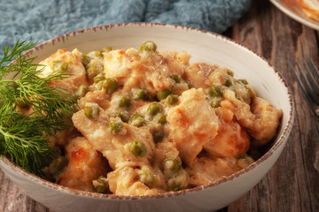 Braised chicken fillet with green peas on a wooden table