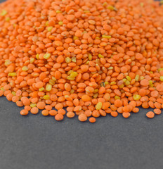 Heap of orange lentil seeds gathered together before a dark gray background