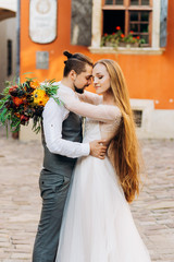 Amazing young couple hugging each other in the yard on a background of orange building. Charming girl with long hair