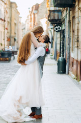 Handsome groom holds his bride in hands on morning street background