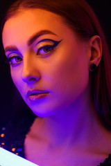 Toned portrait of beautiful woman with neon lamp on dark background