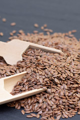 pile of flax or flax seeds in a wooden spoon on a black stone background. dark background Flaxseed concept. vertical photo
