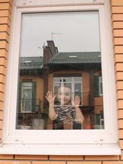 A little girl behind the glass in the house, looking at the street. Quarantine or self-isolation due to the Covid-19 pandemic. Stay at home