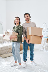 Cheerful young couple in casualwear holding carton boxes with packed stuff