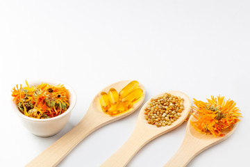 Herbal capsule, natural vitamins, dry calendula flowers at wooden spoon on white background. Concept of healthcare and alternative medicine: homeopathy and naturopathy. Close up, copy space for text