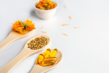 Herbal capsule, natural vitamins, dry calendula flowers at wooden spoon on white background. Concept of healthcare and alternative medicine: homeopathy and naturopathy. Close up, copy space for text