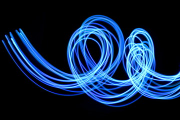 Long exposure photograph of neon blue streaks of light in an abstract swirl, parallel lines pattern against a black background. Light painting photography.