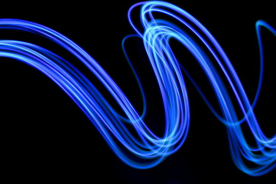 Long exposure photograph of neon blue streaks of light in an abstract swirl, parallel lines pattern against a black background. Light painting photography.