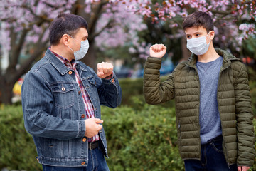 father and son with a face mask shake hands in the city outdoor, blooming trees, spring season, flowering time - concept of allergies and health protection from dusty air