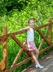 Portrait of beautiful young positive girl in park with braids and red flower in summertime on background of green vegetation in the park near of wooden fence