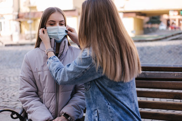 Girls in masks. Coronavirus theme. Women in the city walks during quarantine. Help to put on a mask