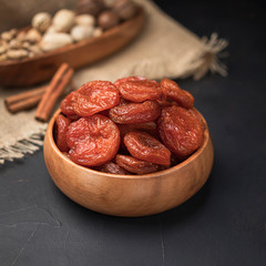 dried fruit in a square wooden bowl on a dark background and burlap