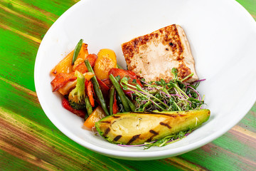 Fried tofu with grilled avocado and wok vegetables. On a colored wooden background. Vegetarian dish.
