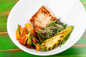 Fried tofu with grilled avocado and wok vegetables. On a colored wooden background. Vegetarian dish.