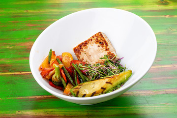 Fried tofu with grilled avocado and wok vegetables. On a colored wooden background. Vegetarian dish.