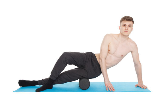 Handsome man shows exercises using a foam roller for a myofascial release massage of trigger points. Isolated on white.