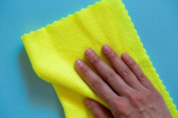 The concept of cleaning and washing. A yellow microfiber rag for cleaning in female hands on a blue...