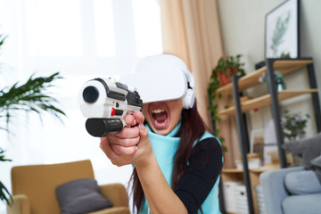 Woman with virtual reality headset and blaster is playing game.