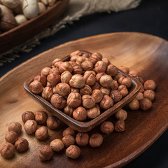 nuts on a square wooden bowl and an oval wooden tray on a dark background and burlap