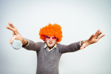 A man in a wig, and sunglasses singing into a microphone.