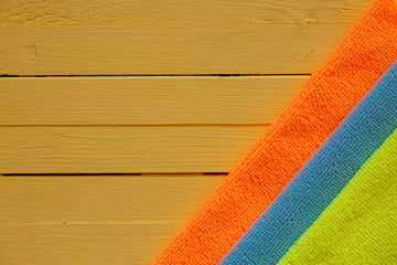 The concept of cleaning and washing. Mix of colored microfiber rags for cleaning on a yellow wooden...
