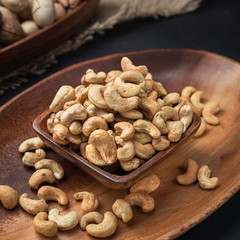 nuts on a square wooden bowl and an oval wooden tray on a dark background and burlap