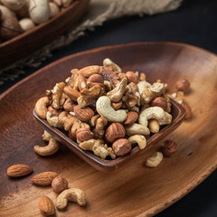 nuts on a square wooden bowl and an oval wooden tray on a dark background and burlap