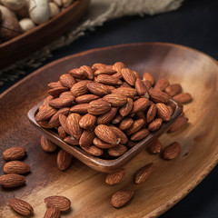 nuts on a square wooden bowl and an oval wooden tray on a dark background and burlap