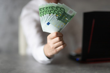 Nominały 100 Euro trzymane w dłoni przez mężczyzne przy laptopie. Koncepcja oferty bankowej, pożyczki, kredytu. - obrazy, fototapety, plakaty