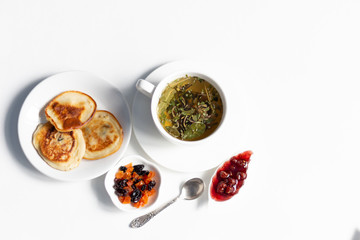 Raspberry jam, dry fruits, fritters, cup of herbal tea, spoon on white background
