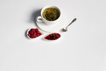Raspberry jam, fresh berries, cup of herbal tea, spoon on white background